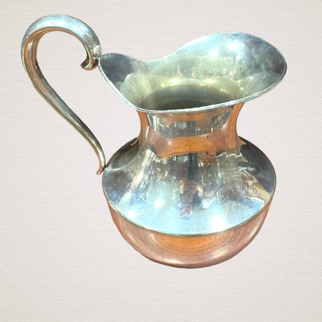 Jarra elegante de metal plateado con diseño curvo y acabado brillante, ideal para decoración de comedor o mesa en estilo clásico.