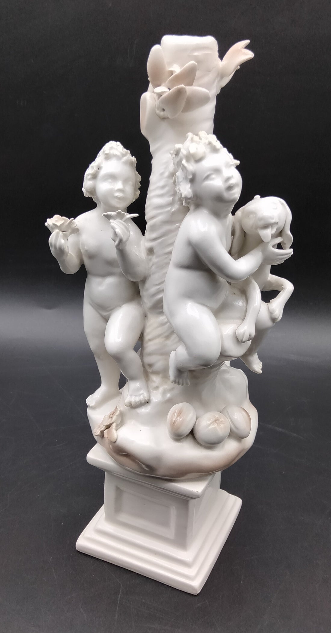 Figura Niños Jugando con Perro - Figura | Porcelana Alemana con dos niños y un perro junto a un tronco decorativo, ideal para decoración de interiores.