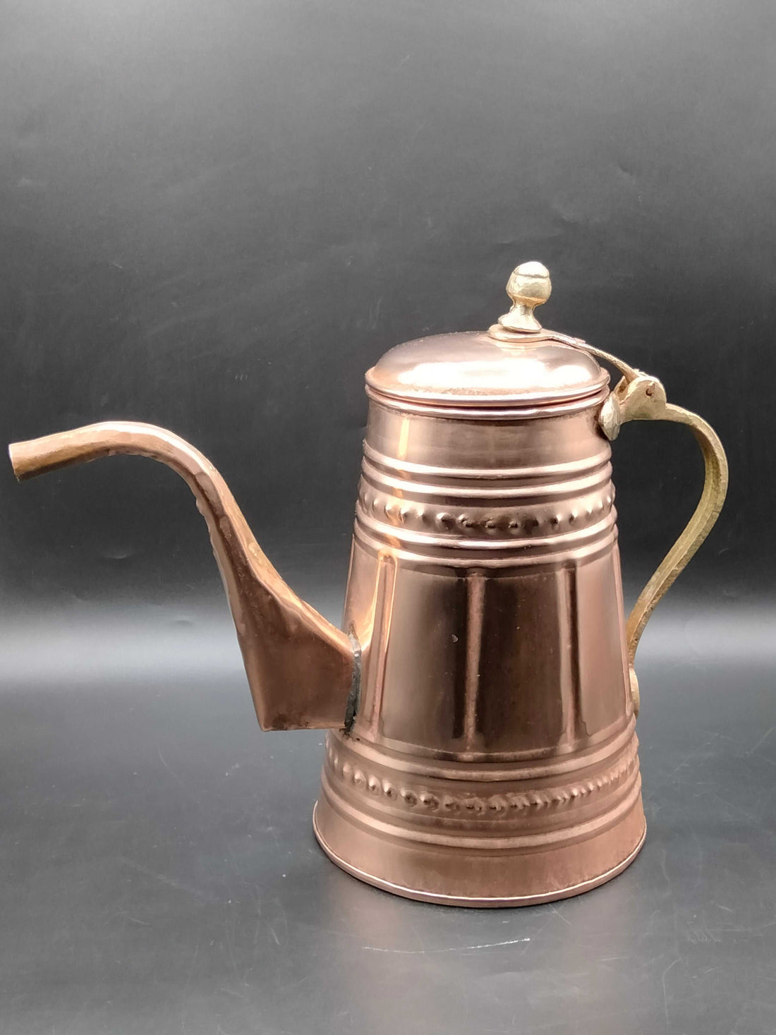 Cafetera de cobre con mango metálico, decorada con relieves artesanales, ideal para decoración vintage en cocina o sala de estar.