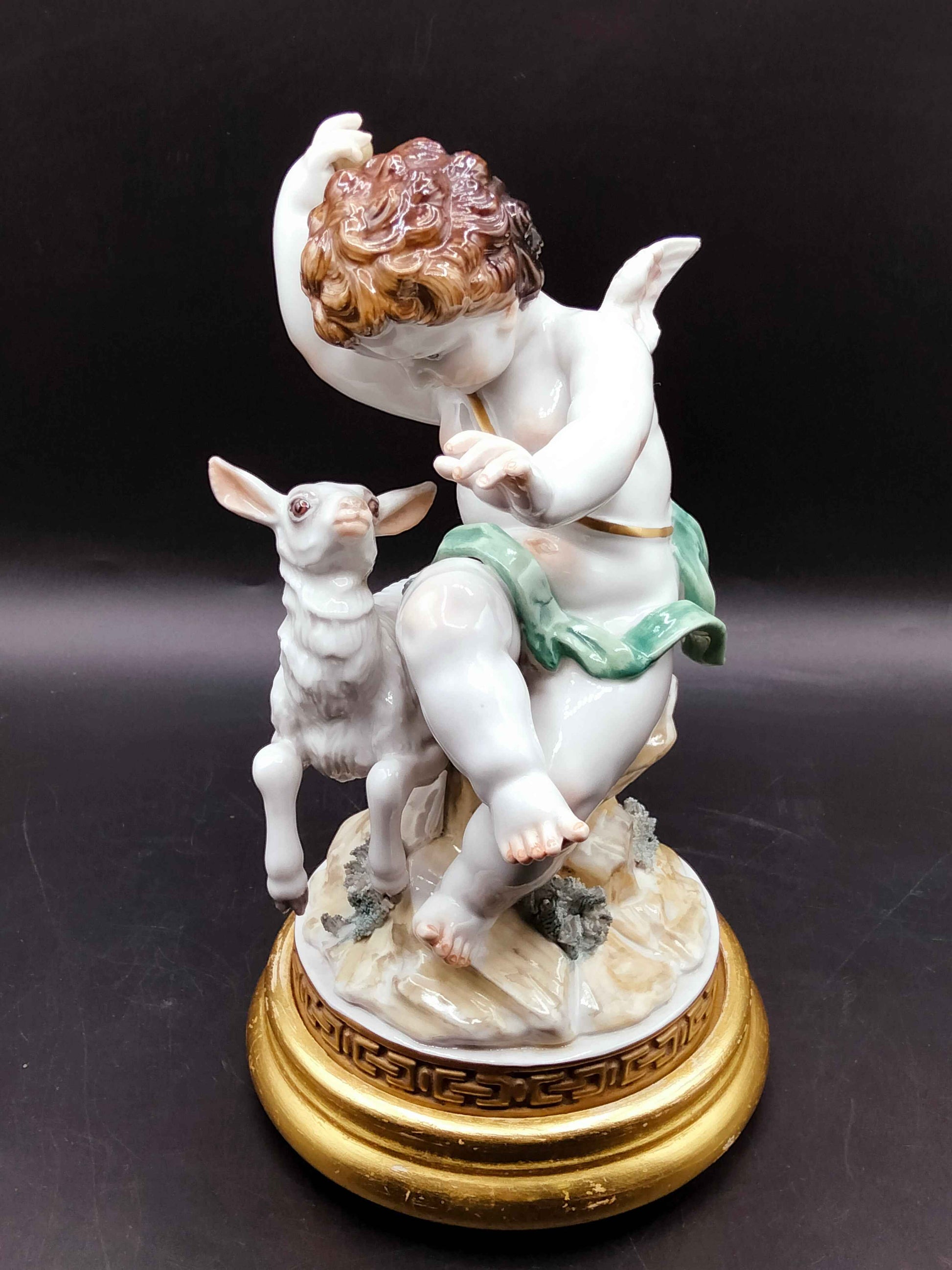 Ángel con borreguito de Algora en pose dinámica, acabado en porcelana esmaltada y base dorada. Decoración de lujo para interiores refinados.