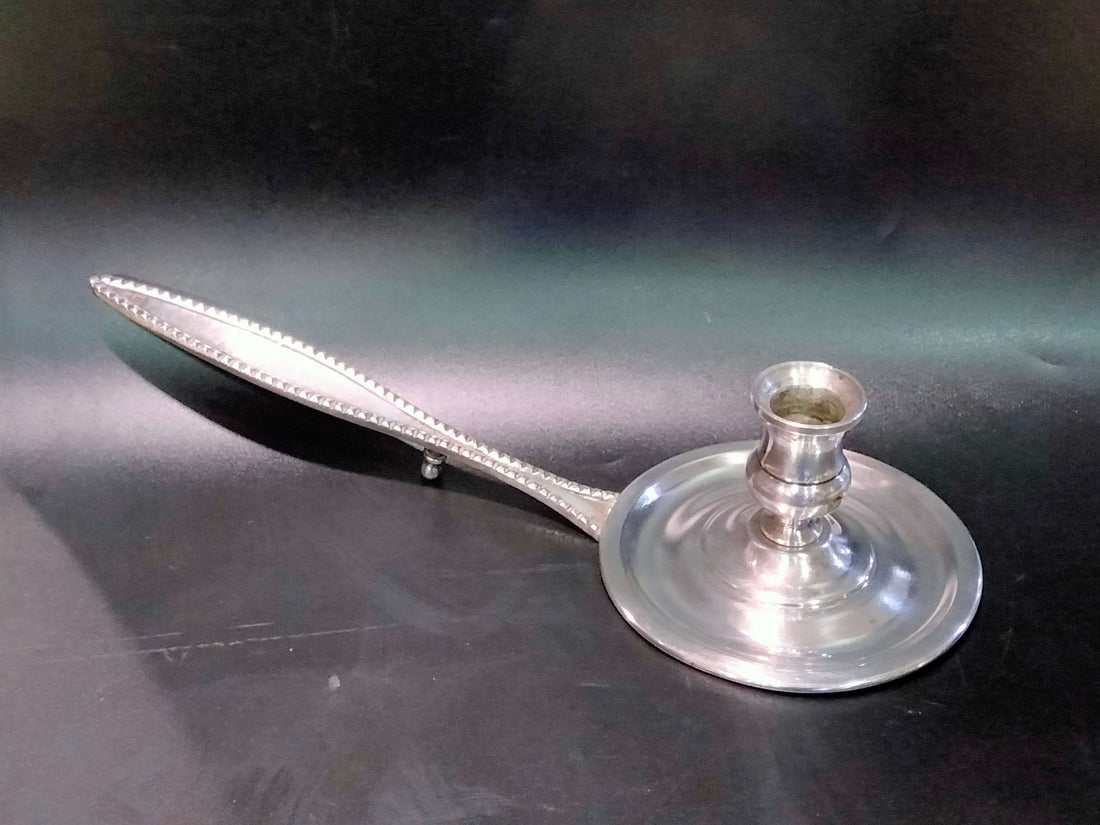 Elegante palmatoria de metal plateado con diseño vintage y brazo largo decorativo. Ideal para decoración clásica en el hogar o jardín.