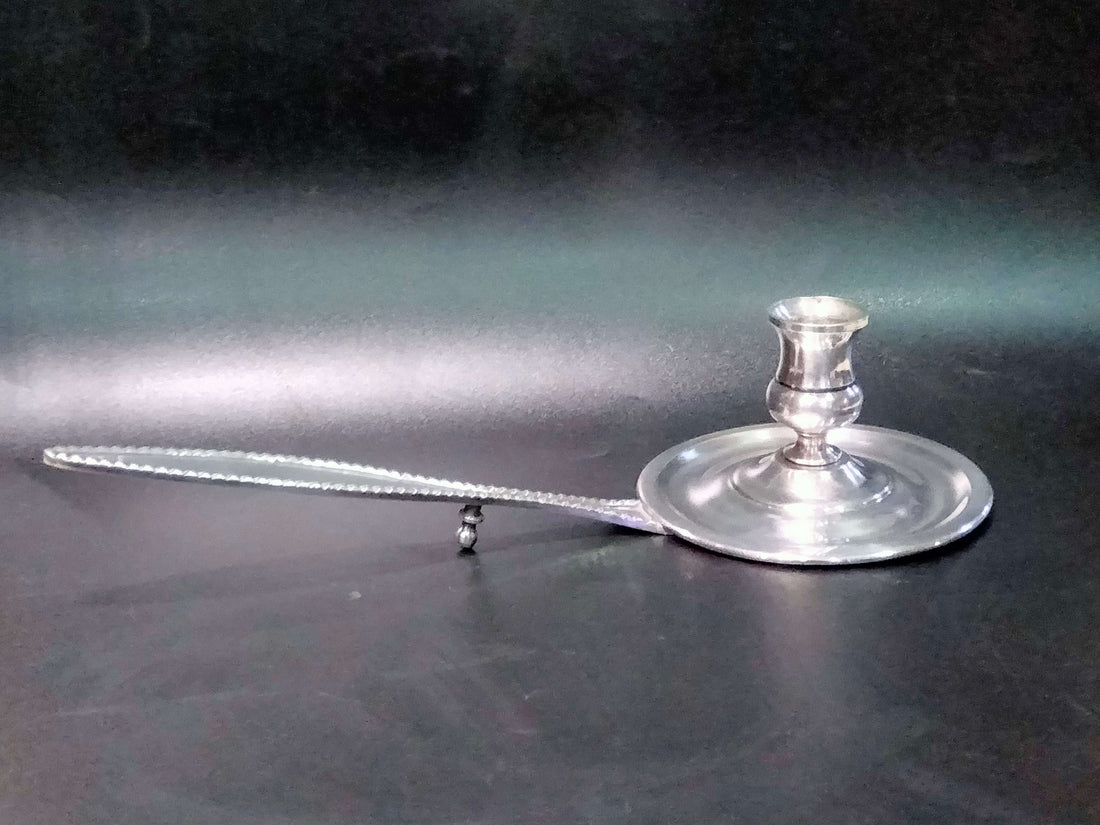 Elegante palmatoria de metal plateado con diseño vintage y brazo largo decorativo. Ideal para decoración clásica en el hogar o jardín.