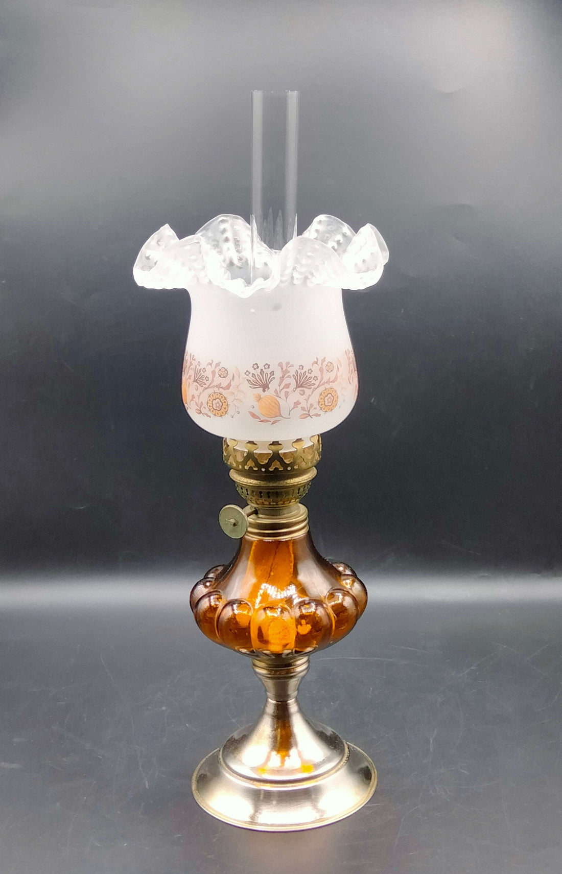 Quinque de cristal ámbar con base metálica y pantalla decorativa floral, estilo años 60, decoración ideal para tu hogar vintage.