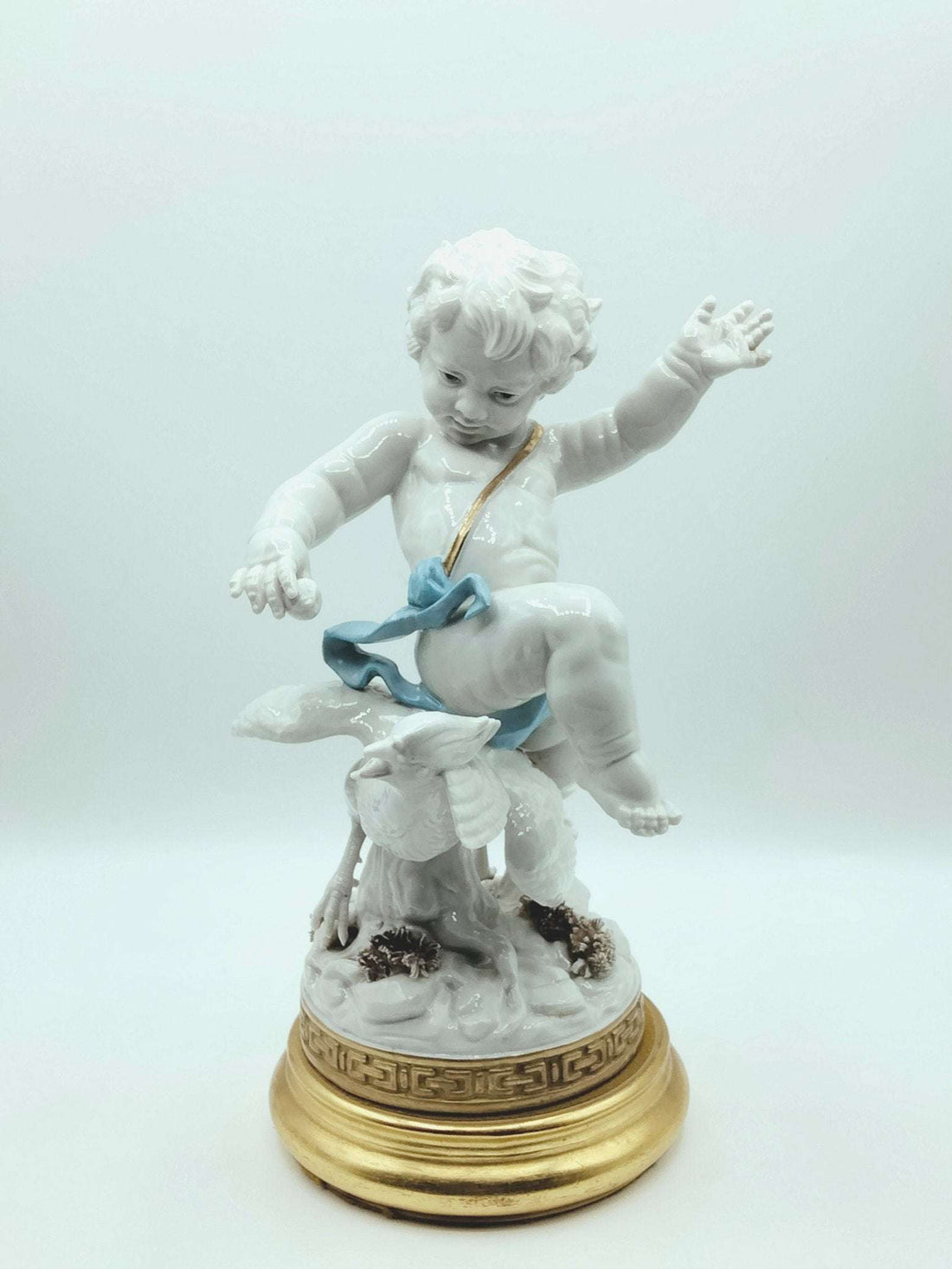 Figura decorativa Angel Blanco Algora cabalgando un faisán, elaborada en porcelana de alta calidad con base dorada. Ideal para decoración de lujo.