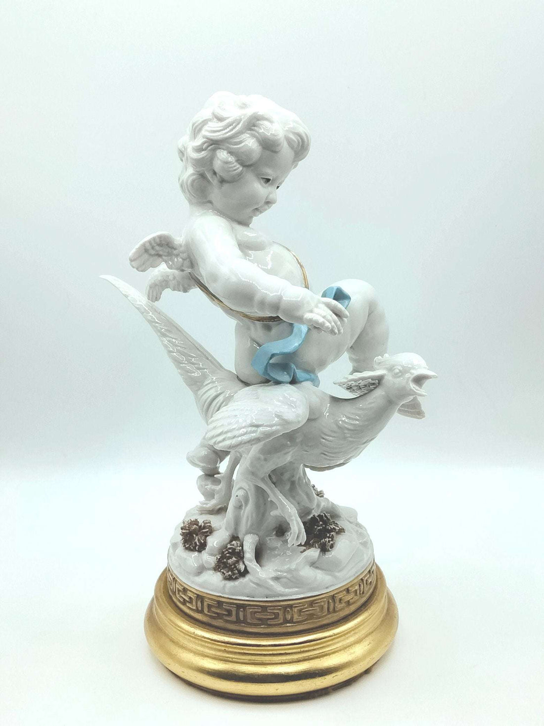Figura decorativa Angel Blanco Algora cabalgando un faisán, elaborada en porcelana de alta calidad con base dorada. Ideal para decoración de lujo.