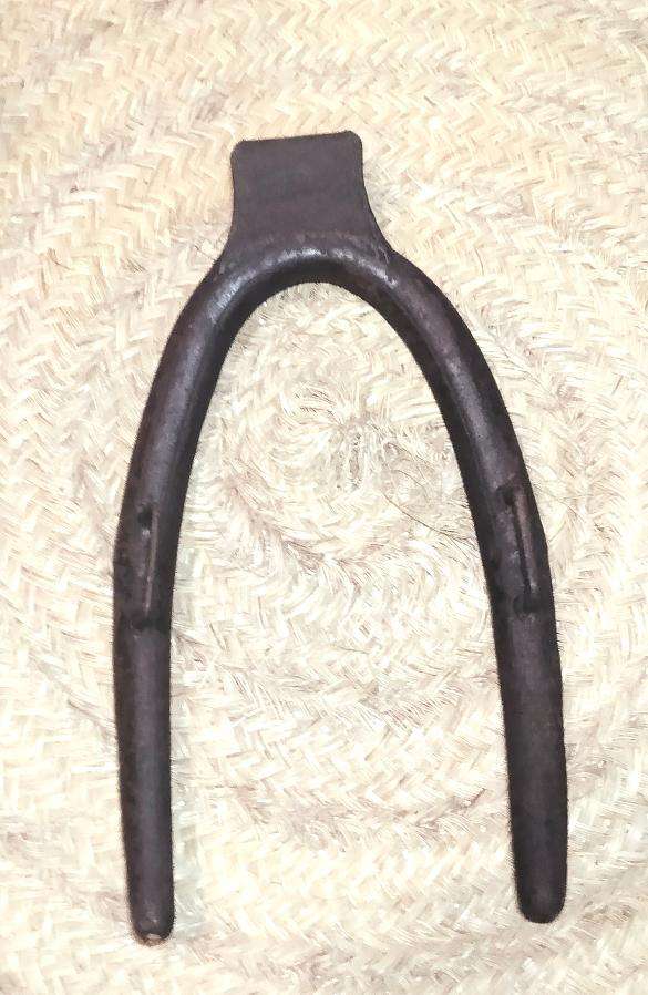 Horcate aéreo de hierro en herradura para caballerías sobre fondo de mimbre, ideal para decoración rústica en establos o casas rurales.