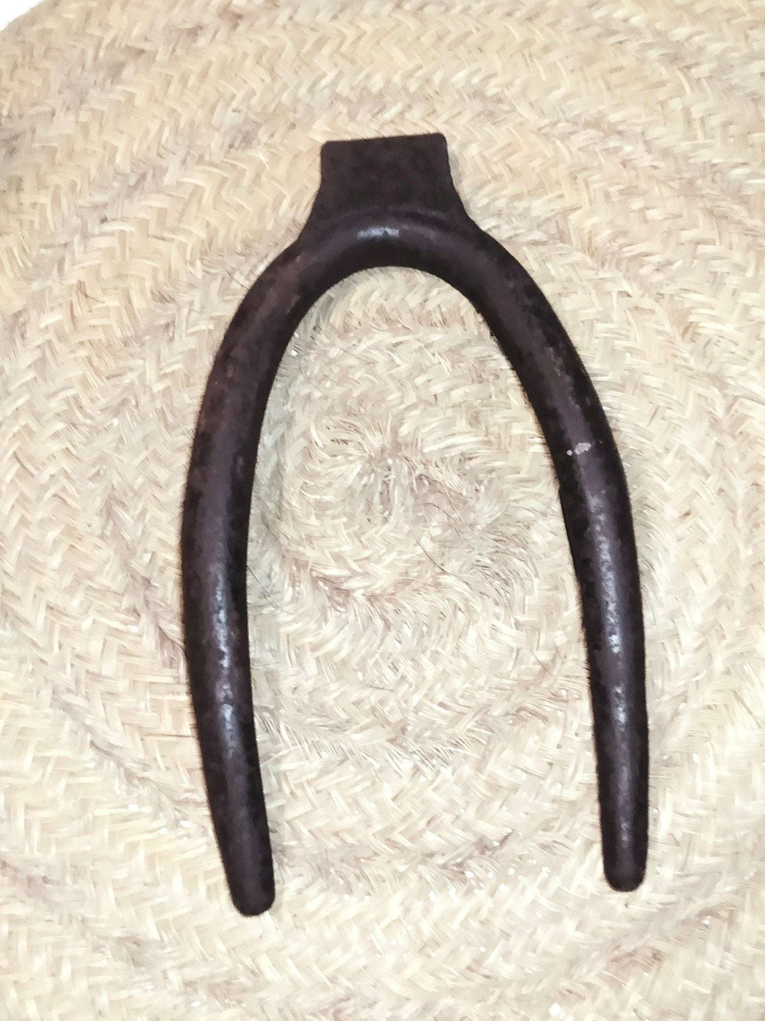 Horcate aéreo de hierro en herradura para caballerías sobre fondo de mimbre, ideal para decoración rústica en establos o casas rurales.