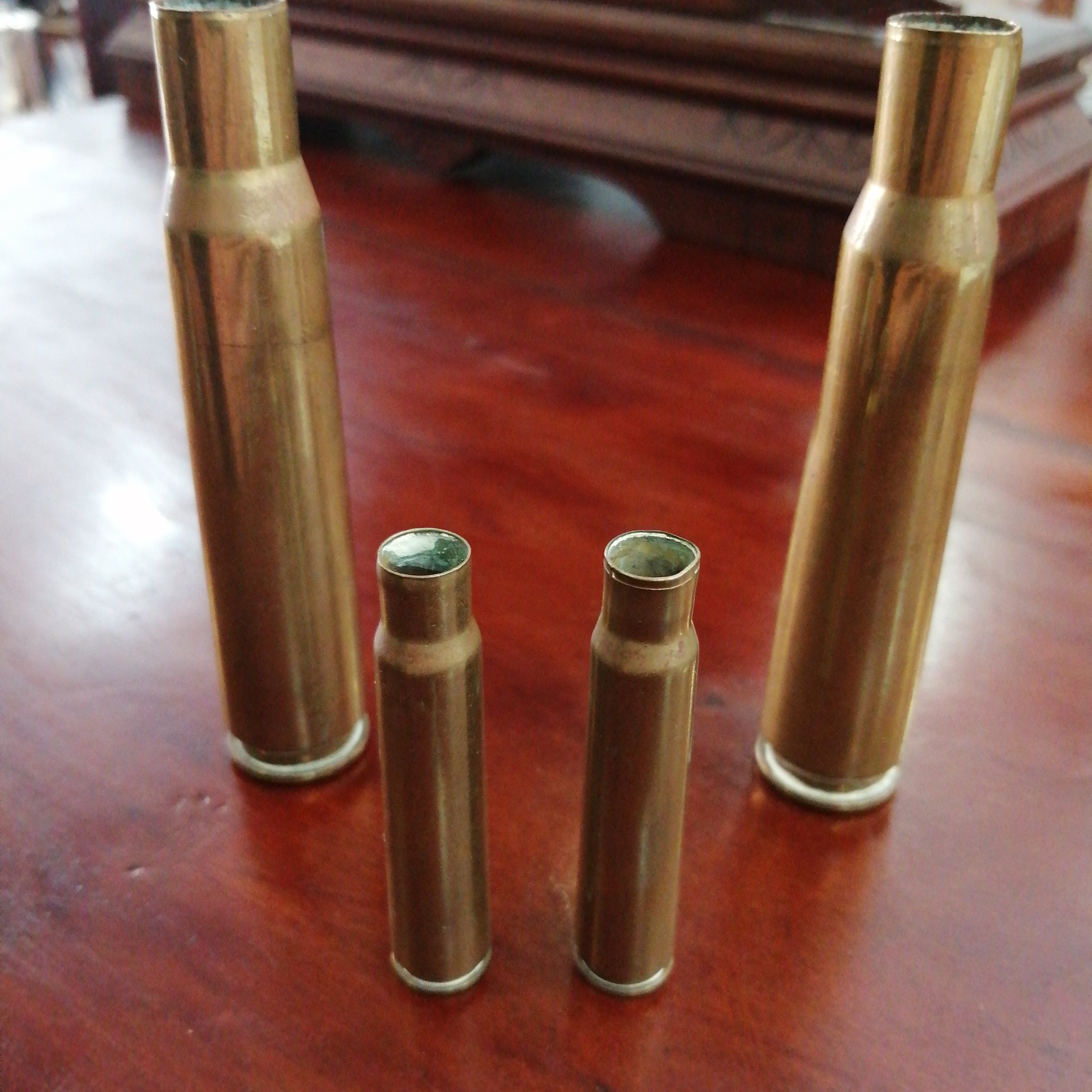 Vainas de proyectil inerte de 10 cm y 5,5 cm sobre mesa de madera, piezas de colección militar vintage para decoración.