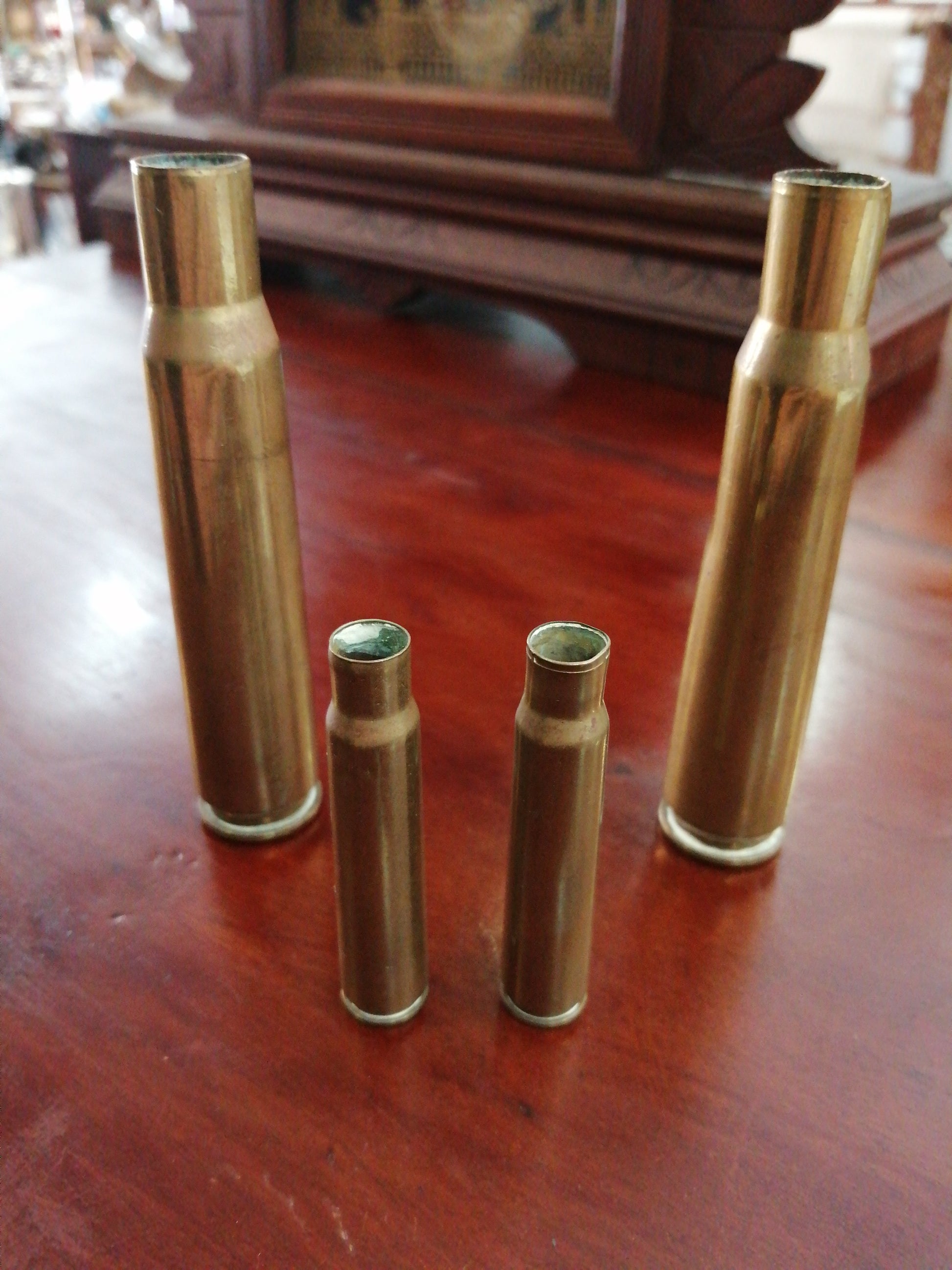 Vainas de proyectil inerte de 10 cm y 5,5 cm sobre mesa de madera, piezas de colección militar vintage para decoración.