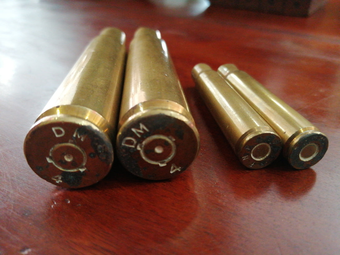 Vainas de proyectil inerte de 10 cm y 5,5 cm sobre mesa de madera, piezas de colección militar vintage para decoración.