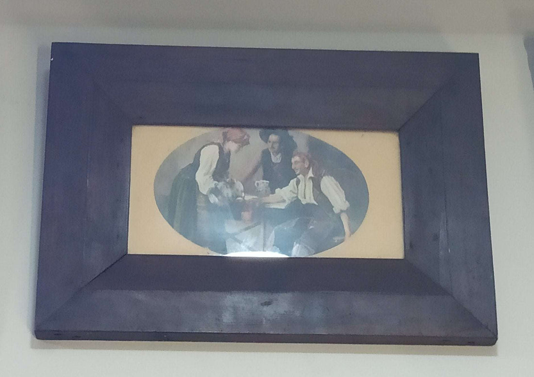 Lamina antigua de escena rural con marco de caoba, muestra a dos hombres y una mujer sirviendo una jarra en un entorno costumbrista. Ideal para decoración vintage en hogar o jardín.