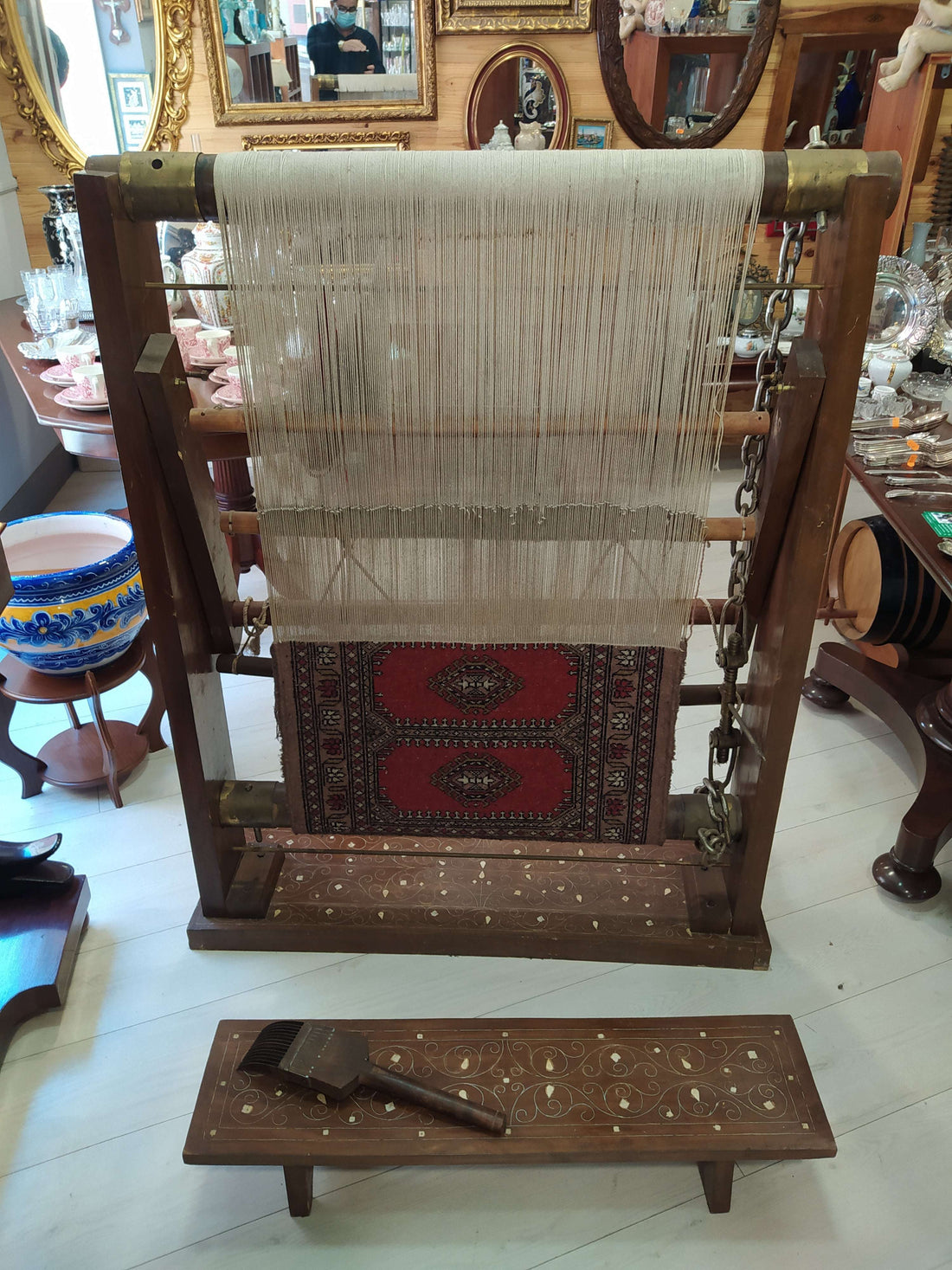 Telar antiguo con alfombra en proceso, estructura de madera con incrustaciones de nácar y banqueta decorativa, ideal para decorar con estilo vintage.