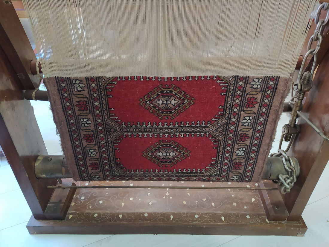 Telar antiguo con alfombra en proceso, estructura de madera con incrustaciones de nácar y banqueta decorativa, ideal para decorar con estilo vintage.