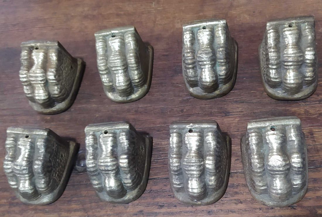Juego de 8 garras de metal para patas de mesas antiguas, estilo vintage, en acabado dorado envejecido sobre superficie de madera oscura.