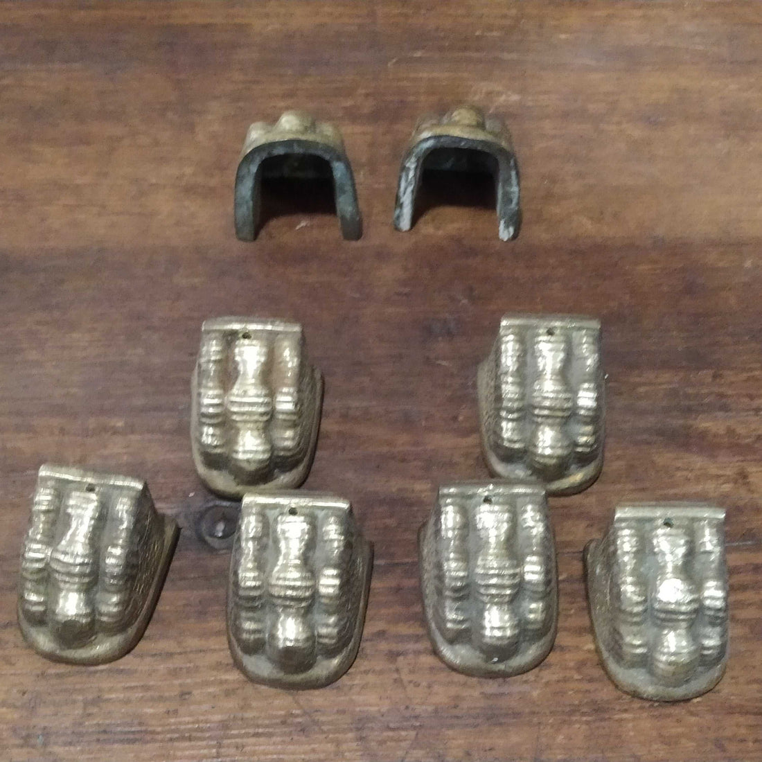 Juego de 8 garras de metal para patas de mesas antiguas, estilo vintage, en acabado dorado envejecido sobre superficie de madera oscura.