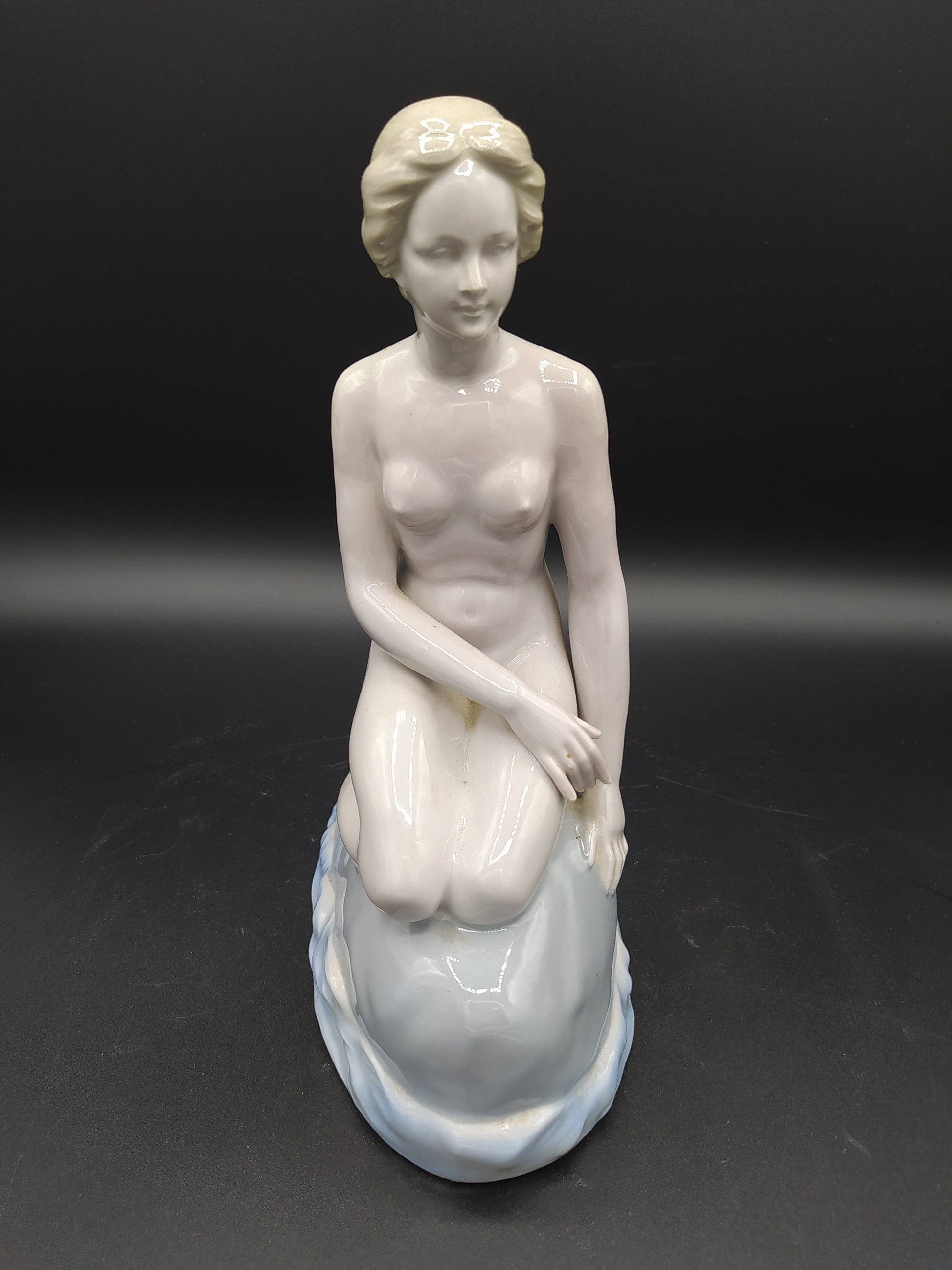 Figura de La Sirenita de porcelana en posición sentada sobre una roca, con acabado brillante y estilo clásico, ideal para decoración vintage.