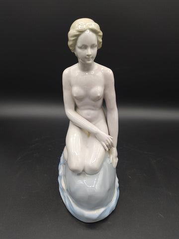 Figura de La Sirenita de porcelana en posición sentada sobre una roca, con acabado brillante y estilo clásico, ideal para decoración vintage.