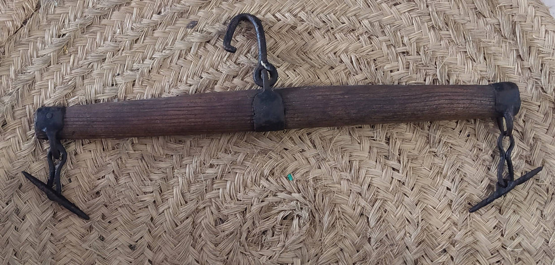 Balancín de madera dura para tiro animal con gancho central y extremos metálicos, ideal para mulas y caballos en decoración rústica.