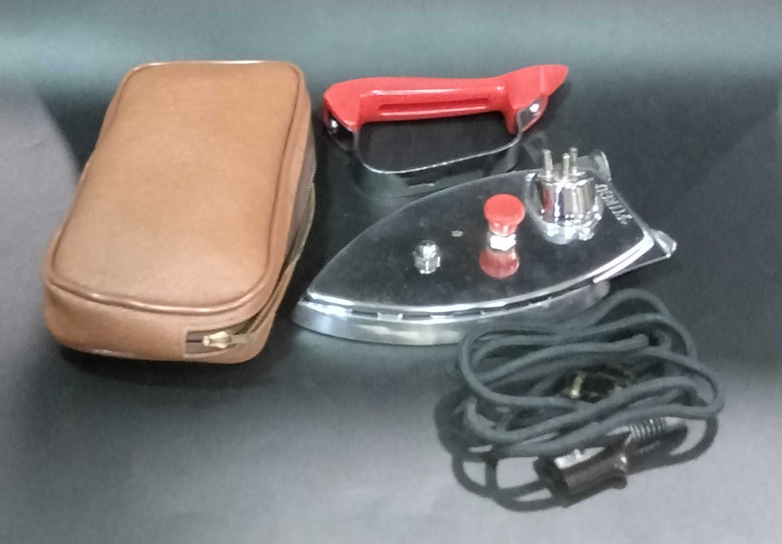 Plancha Eléctrica de Viaje Fuego con mango rojo desmontable, cable negro y estuche marrón. Ideal para coleccionistas y decoración vintage.