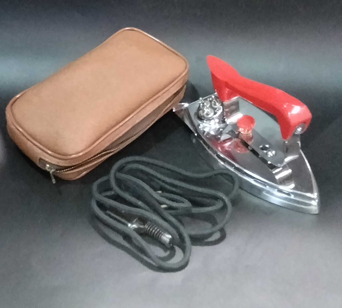 Plancha Eléctrica de Viaje Fuego con mango rojo desmontable, cable negro y estuche marrón. Ideal para coleccionistas y decoración vintage.