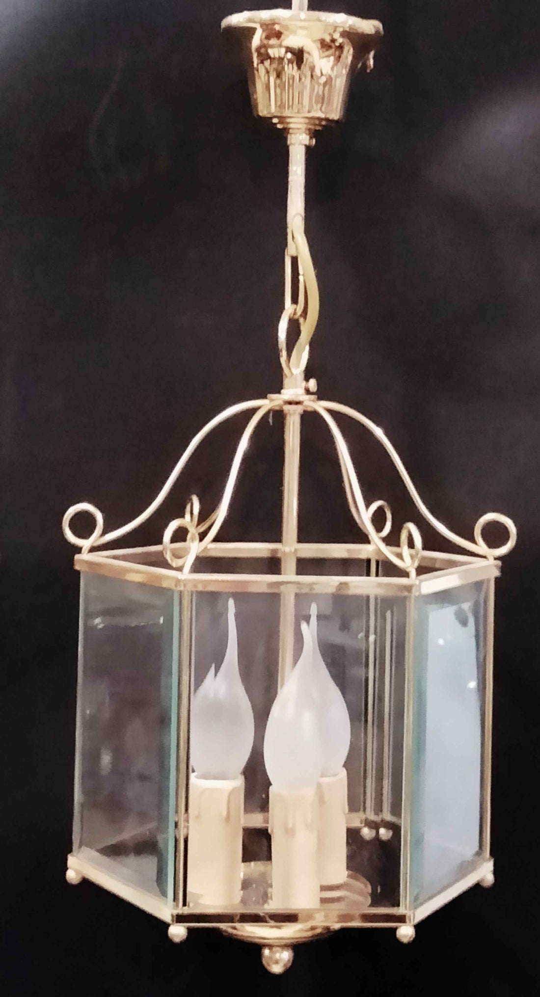 Lámpara farol de bronce dorado con estructura acristalada y 4 luces eléctricas tipo vela. Ideal para decoración de pasillos o entradas elegantes.
