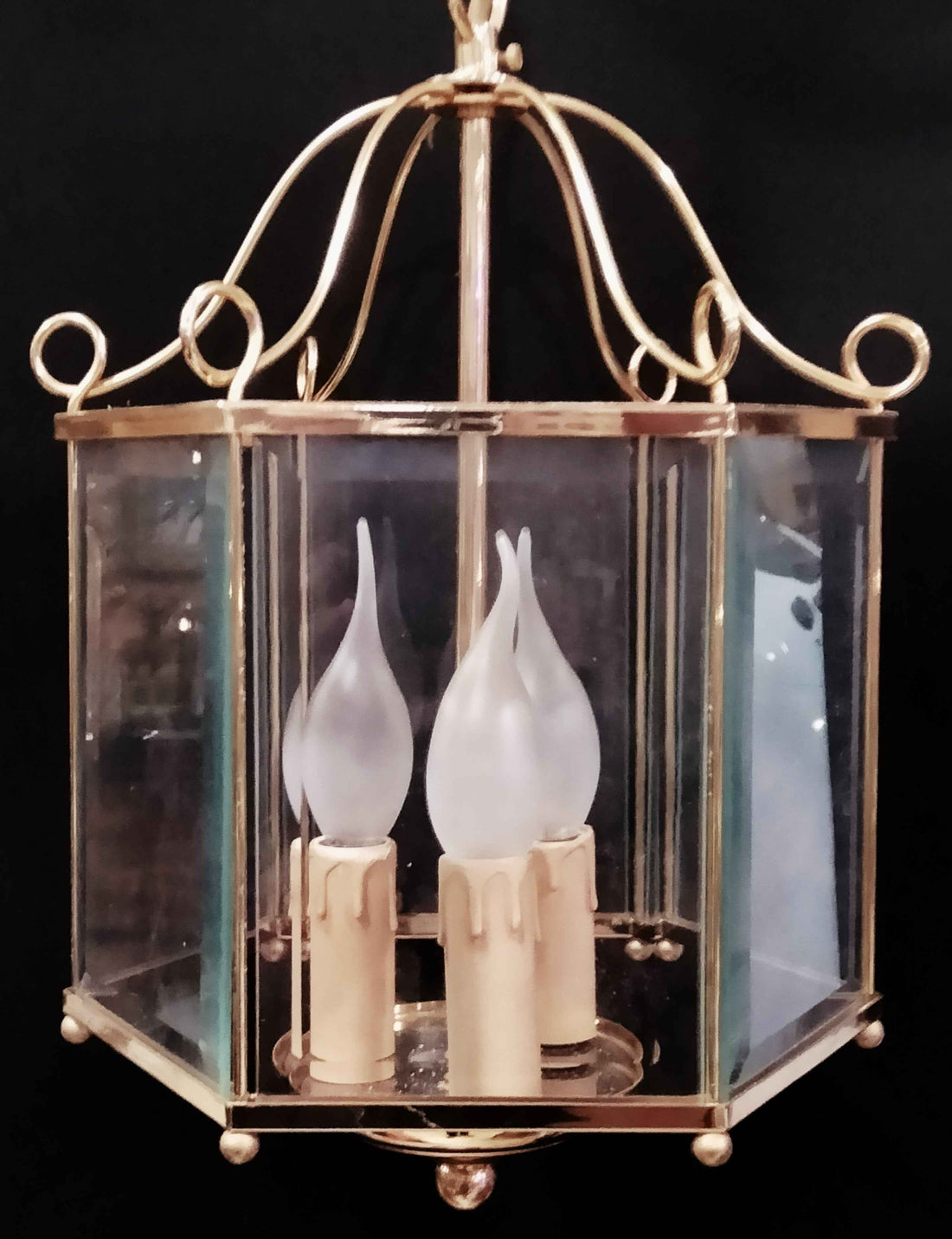 Lámpara farol de bronce dorado con estructura acristalada y 4 luces eléctricas tipo vela. Ideal para decoración de pasillos o entradas elegantes.