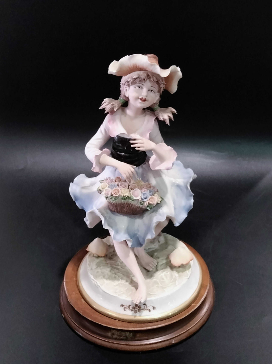 Figuras de porcelana fina marca Carlos | Niño con instrumento y niña con flores sobre metopas de madera, decoración elegante para el hogar.