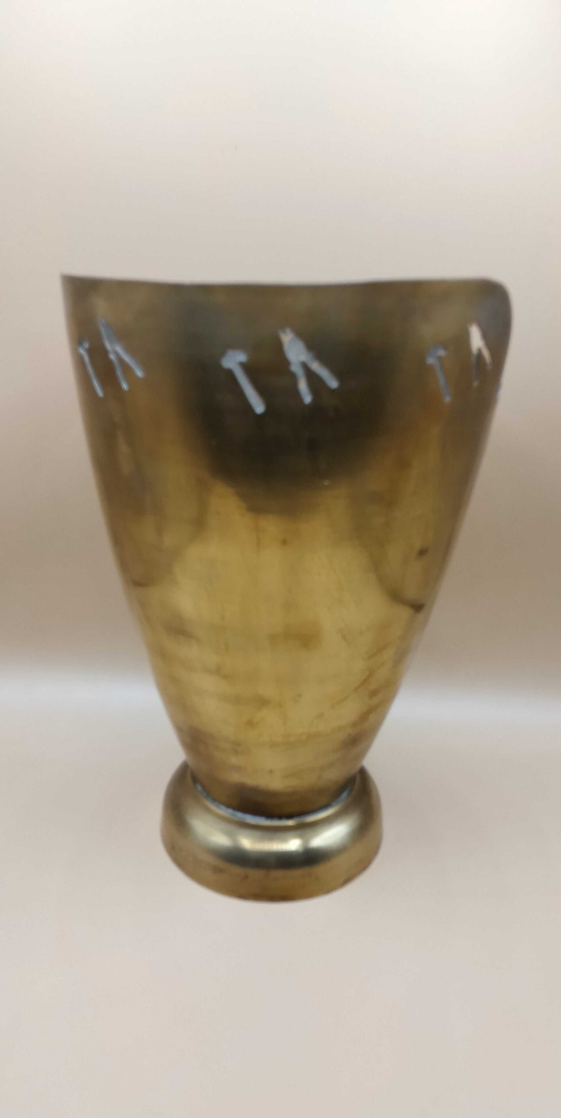 Jarrón de metal con detalles artesanales, único en su estilo, acabado dorado y figuras recortadas de herramientas en la parte superior.