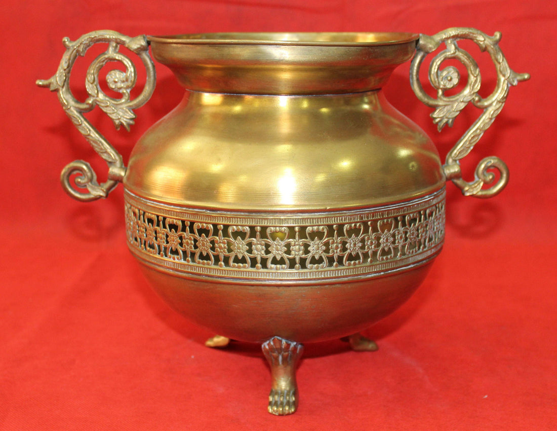 Macetero de metal de alta calidad con asas ornamentadas y diseño floral calado, ideal para decoración vintage en interiores o exteriores.