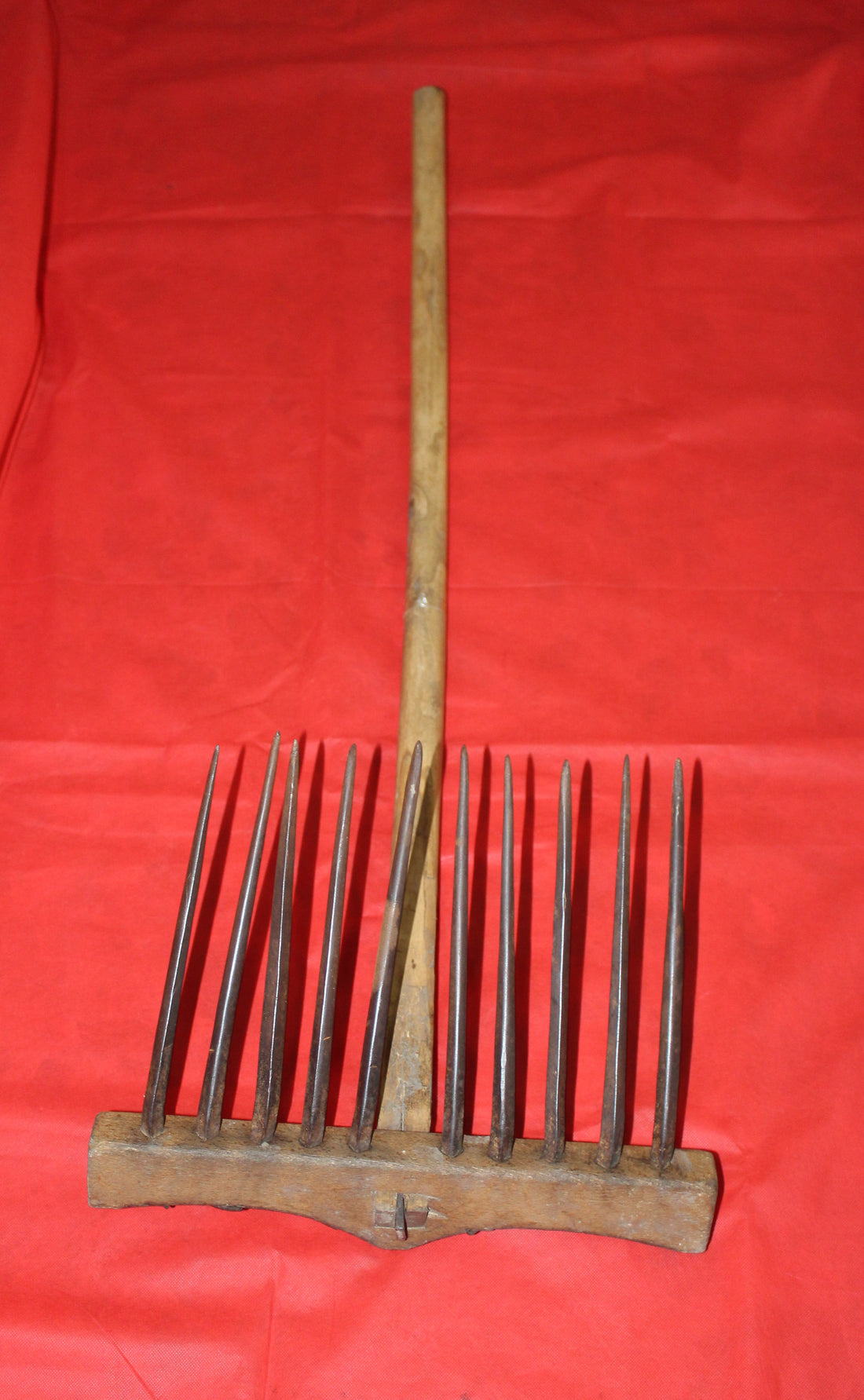 Rastrillo antiguo para campo de hierro y madera sobre fondo rojo, ideal como decoración vintage de jardín o casa rural.