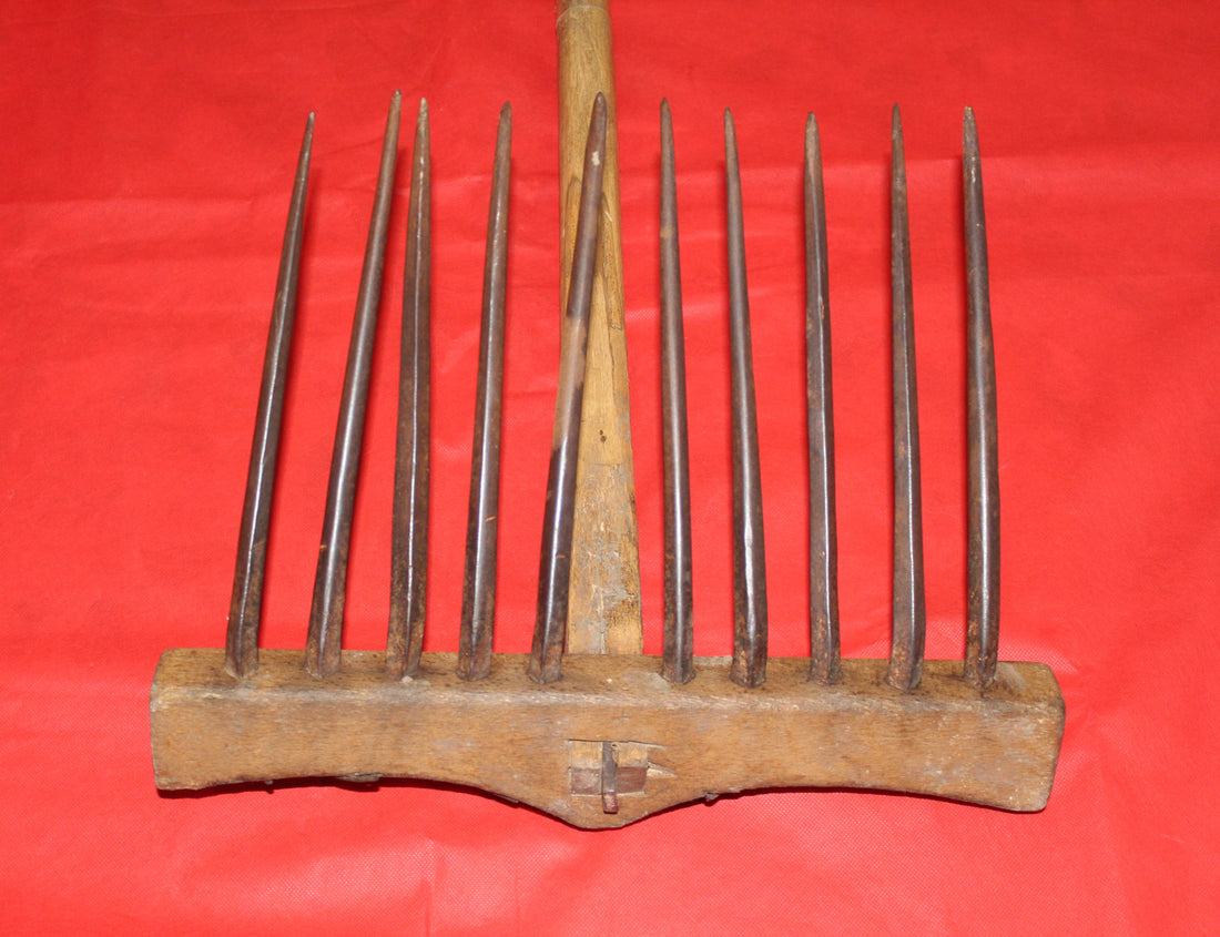 Rastrillo antiguo para campo de hierro y madera sobre fondo rojo, ideal como decoración vintage de jardín o casa rural.