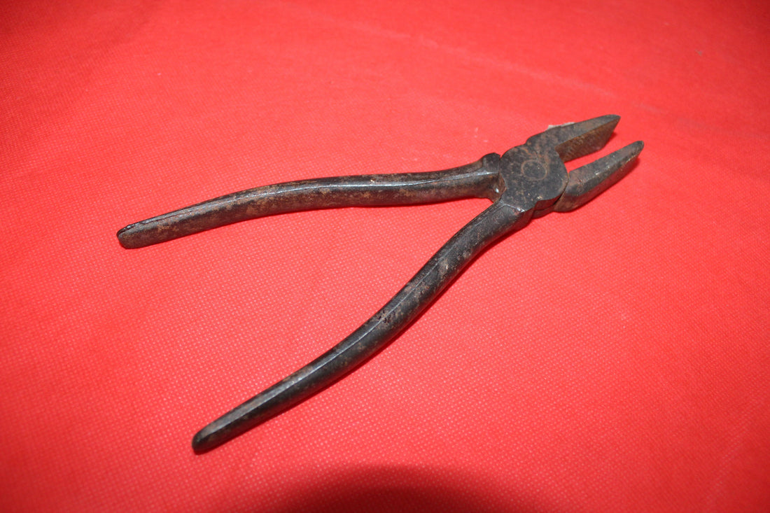 Alicate antiguo de hierro sobre fondo rojo, herramienta de colección de calidad ideal para decoración vintage en hogar o jardín.