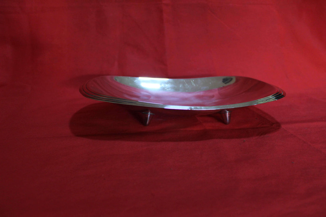 Bandeja con patas de metal plateado de alta calidad sobre fondo rojo, ideal para decoración de interiores o eventos especiales.