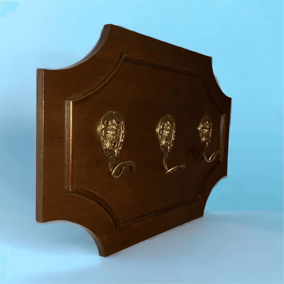 Perchero antiguo de caoba con detalles ecuestres únicos, incluye tres ganchos dorados con forma de herradura sobre fondo azul claro.