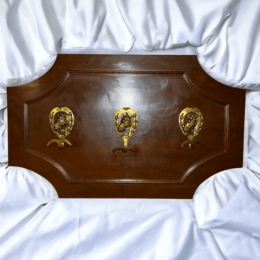 Perchero antiguo de caoba con detalles ecuestres únicos, incluye tres ganchos dorados con forma de herradura sobre fondo azul claro.